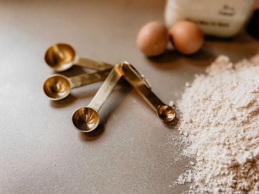 Gold measuring teaspoons beside flour and eggs showing the teaspoon-to-milliliter conversion.